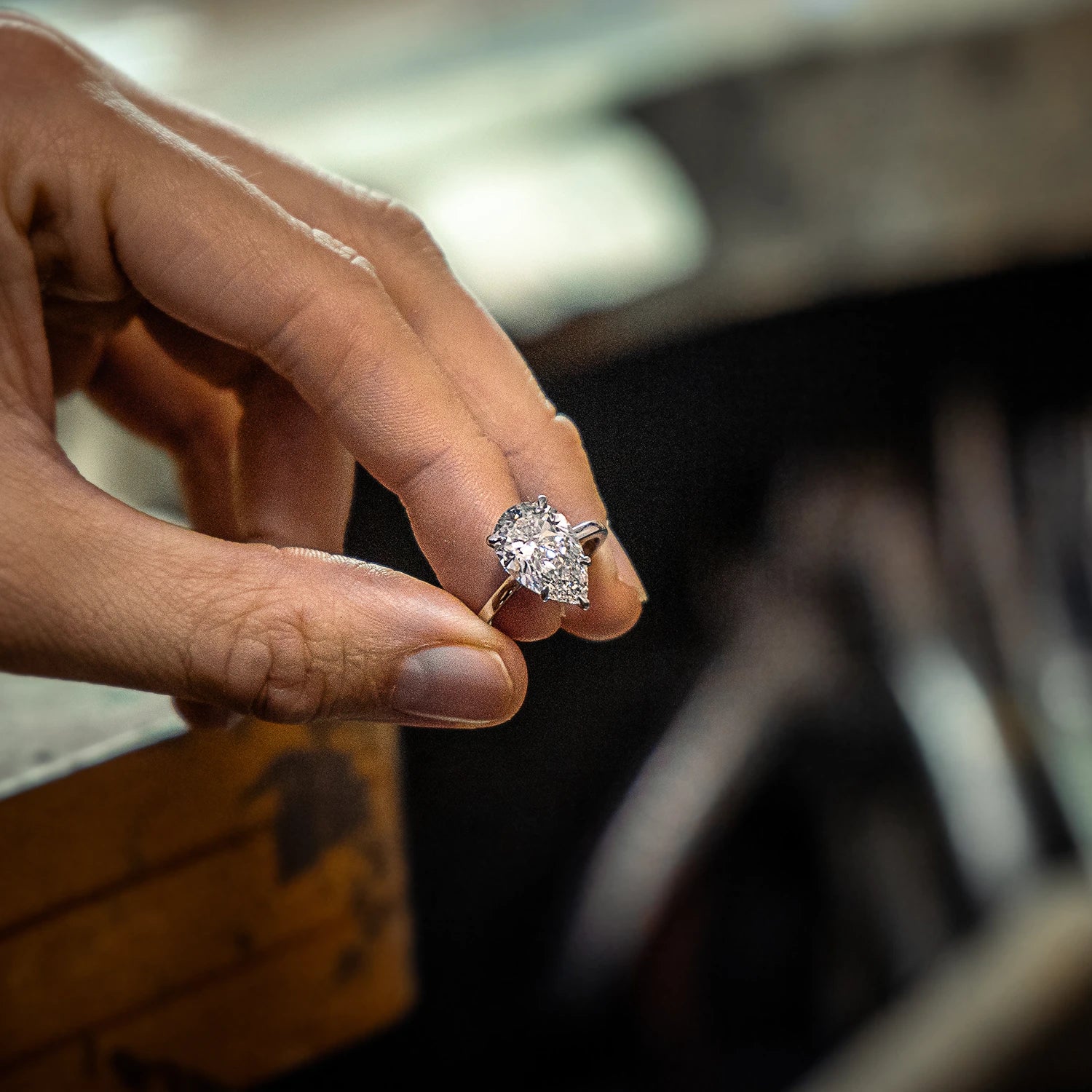 Hand holding a pear-shaped diamond engagement ring with a platinum band, photographed in a York city centre jewellery shop