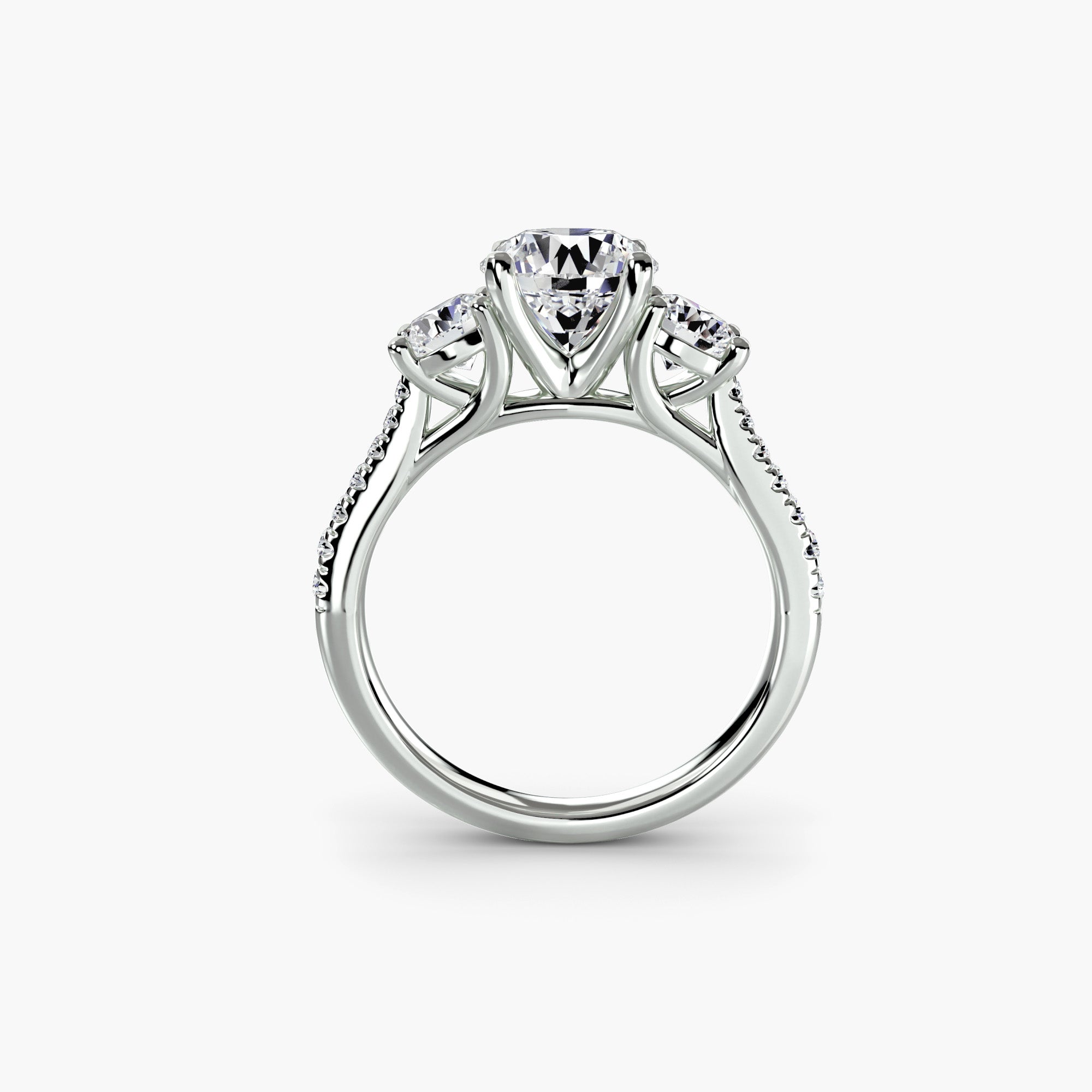 A side view of the MICHAEL ISAAC Three-Stone with Pavé Band shows a silver ring with a large central diamond, two smaller side diamonds, and pavé-set diamonds on the band, displayed against a plain white background.