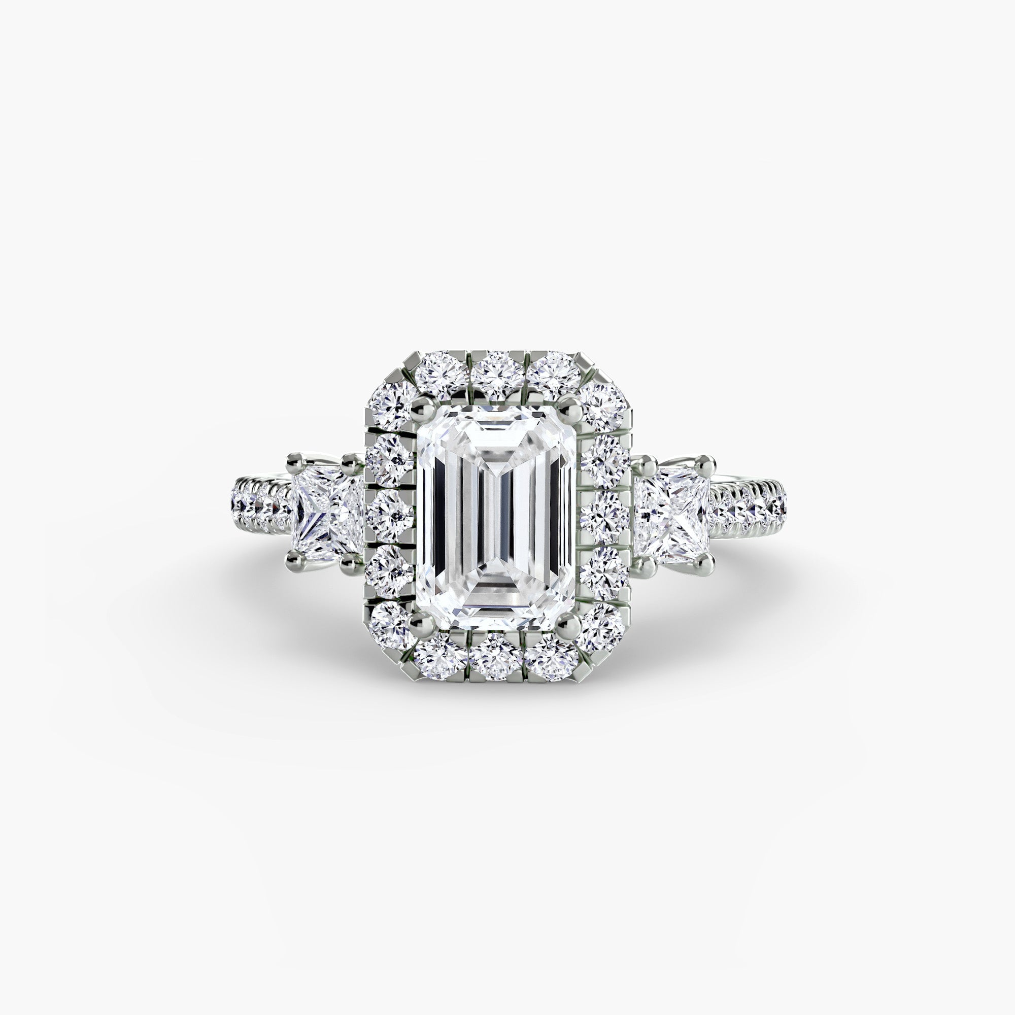 The MICHAEL ISAAC Three-Stone Ring with Halo 2 features a large emerald-cut diamond at the center, accented by a radiant halo of smaller round diamonds and side stones, beautifully displayed on a clean white background.