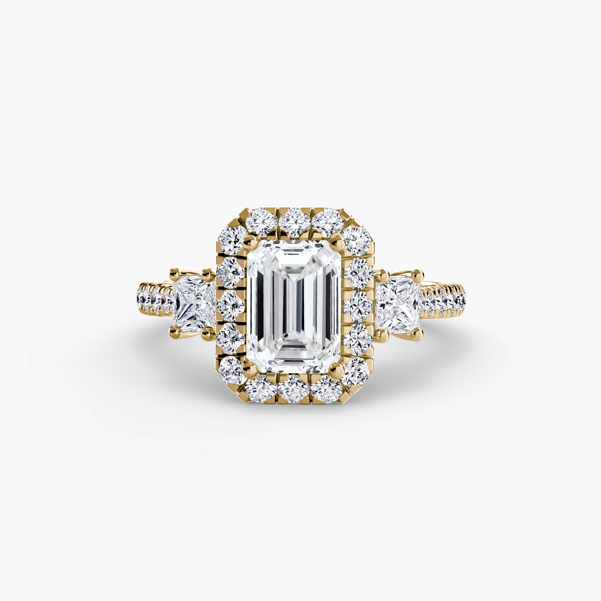 The MICHAEL ISAAC Three-Stone Ring with Halo 2 features a gold band, a rectangular emerald-cut diamond center, radiant halo of small round diamonds, and extra diamonds on the band for a modern touch.