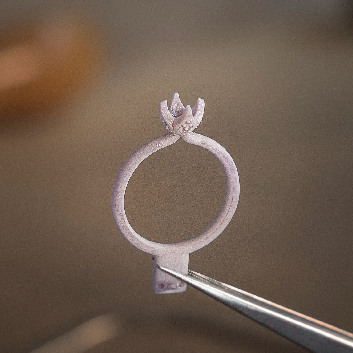 engagement ring with a decorative top held by tweezers against a blurred background