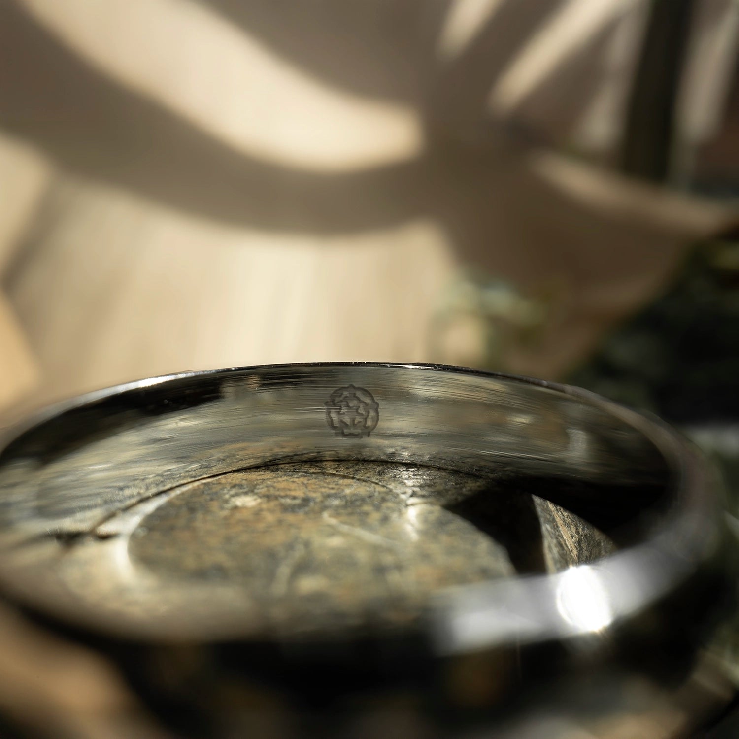 A close-up of the Engagement Ring by MICHAEL ISAAC, featuring a small engraved Yorkshire Rose Stamp on the inner band, set on stone with soft sunlight and shadows in the background