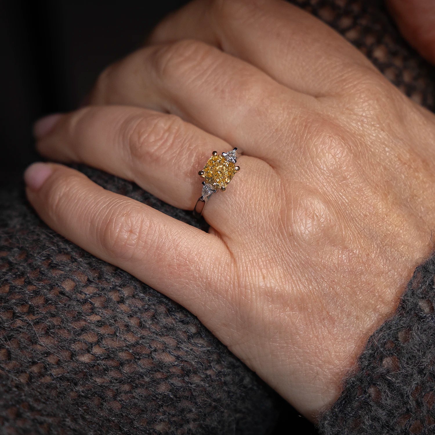 Close-up of a woman’s hand wearing a yellow diamond engagement ring with side stones on a platinum band