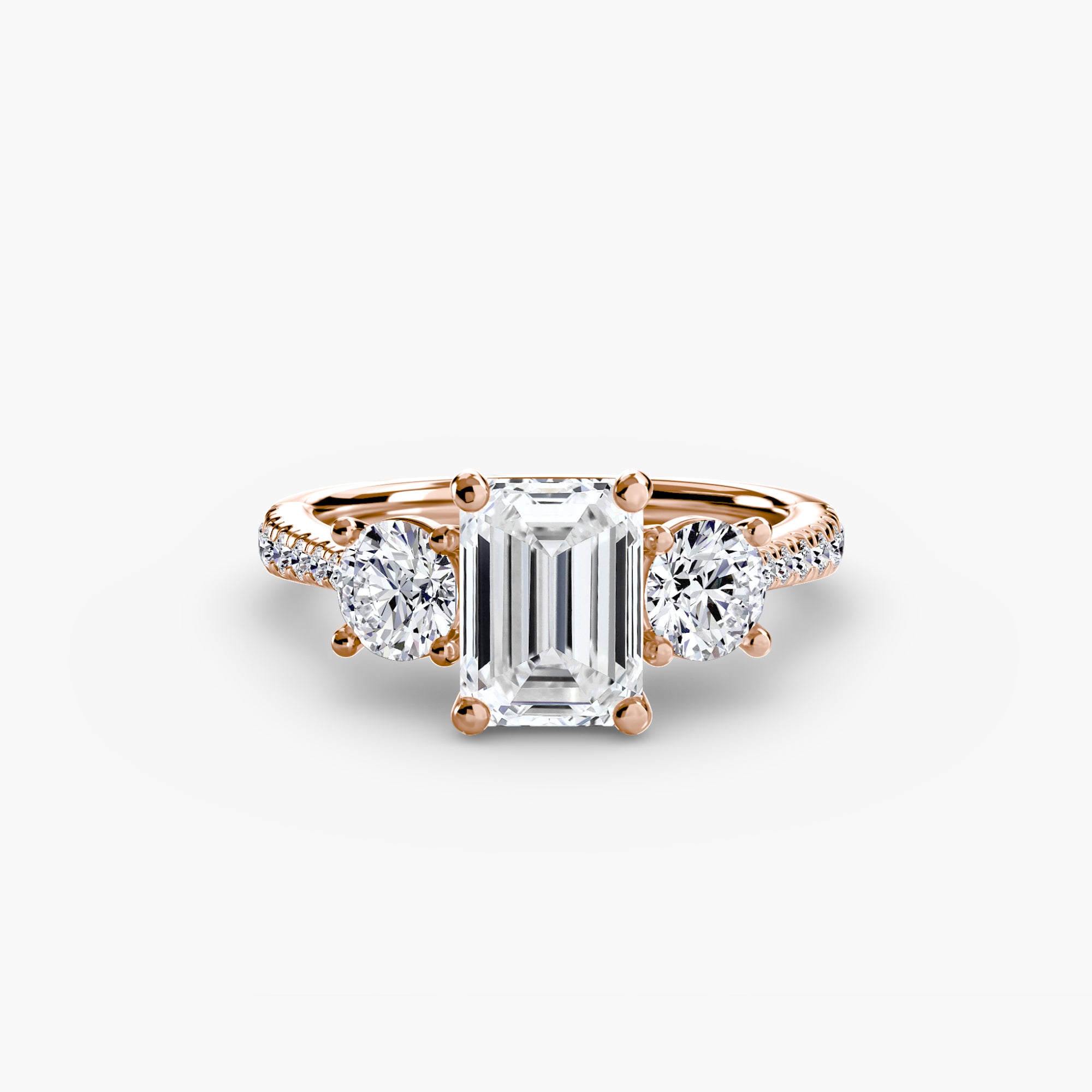 The MICHAEL ISAAC Three-Stone with Pavé Band ring features an emerald-cut center diamond, two round side diamonds, and a rose gold pavé band adorned with sparkling diamonds along the shoulders.