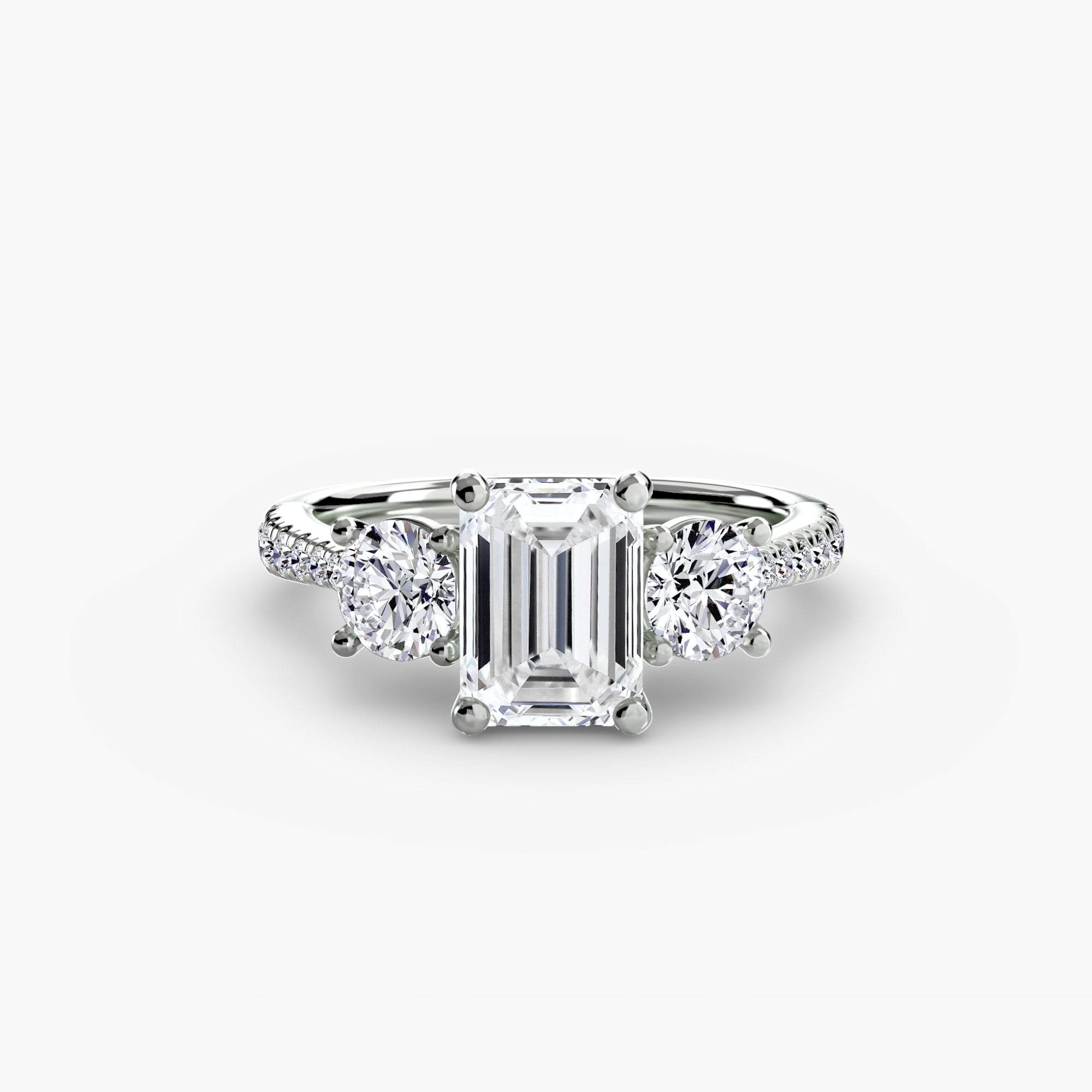 The MICHAEL ISAAC Three-Stone with Pavé Band ring, shown on a plain white background, features an emerald-cut center diamond flanked by two round diamonds and pavé-set diamonds along its white gold band.