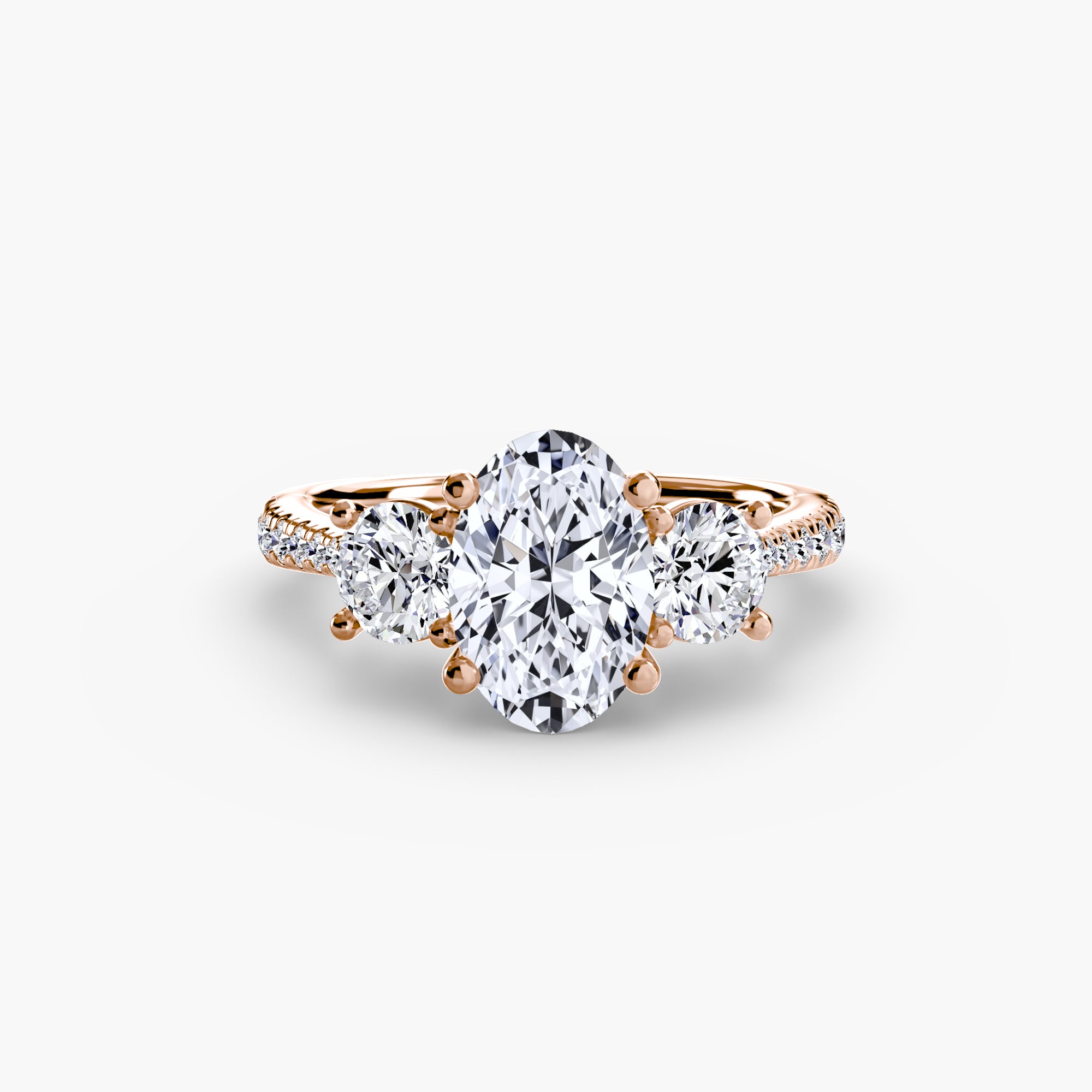 The MICHAEL ISAAC Three-Stone with Pavé Band ring in rose gold showcases an oval center diamond, two round side diamonds, and a pavé-set diamond band, elegantly presented on a plain white background.