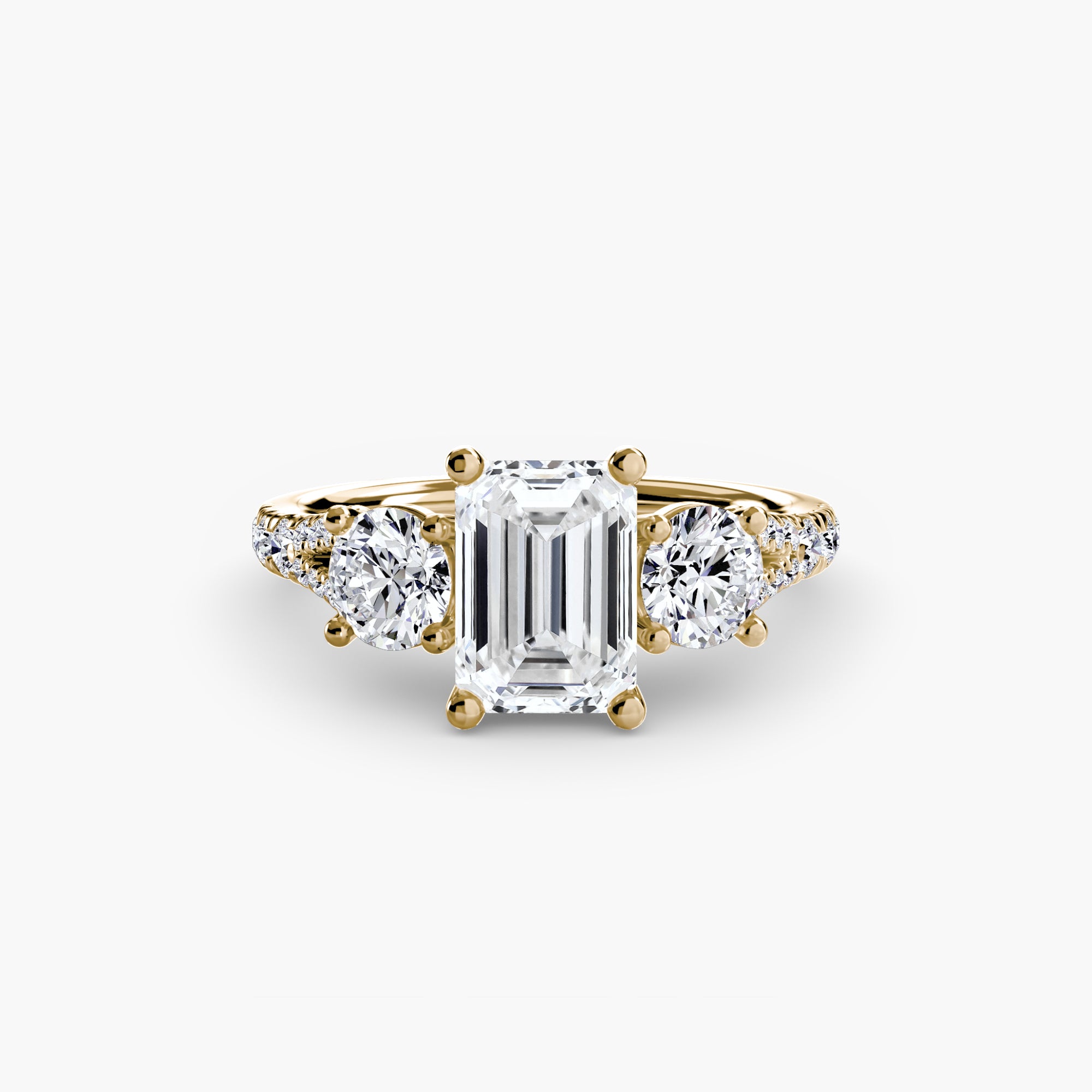 The MICHAEL ISAAC Three-Stone with Pavé Band 3 is a gold ring featuring a central emerald-cut diamond flanked by two round diamonds, displayed on a plain white background.