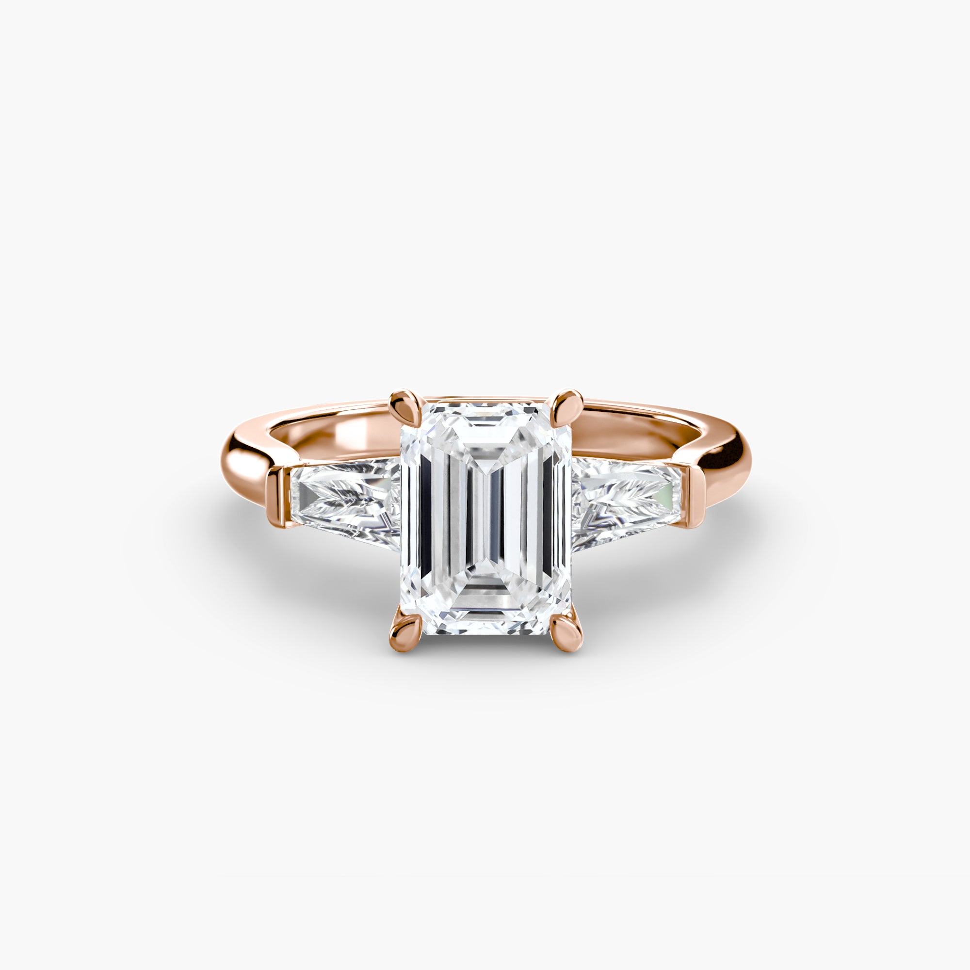 The MICHAEL ISAAC Three-Stone Ring features an emerald-cut diamond center with baguette side stones in rose gold, shown on a white background.