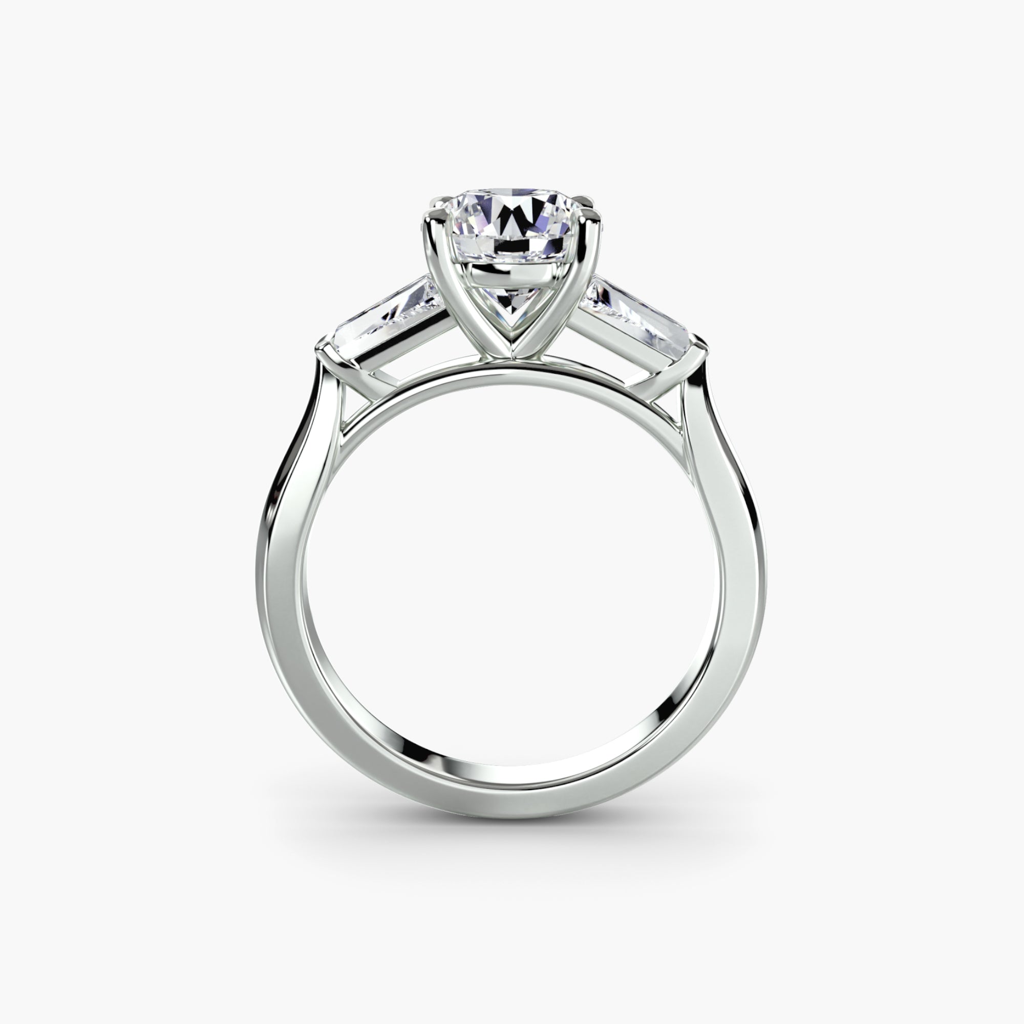 The MICHAEL ISAAC Three-Stone Ring features a round-cut diamond solitaire with baguette side stones in a prong setting, inspired by the classic past present future design, shown from the side against a plain white background.