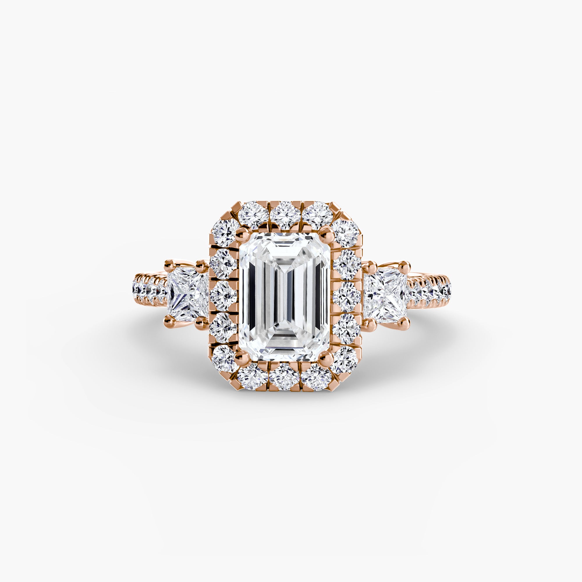 The MICHAEL ISAAC Three-Stone Ring with Halo 2 features an emerald-cut center diamond, a radiant halo of round diamonds, and additional diamonds set along the band and on each side of the main setting.